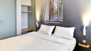 A hotel room with a bed, a nightstand, a wall-mounted TV, and a window with a view of buildings. - B&B HOTEL Toulouse Cité de l'Espace Mouchotte (Toulouse)