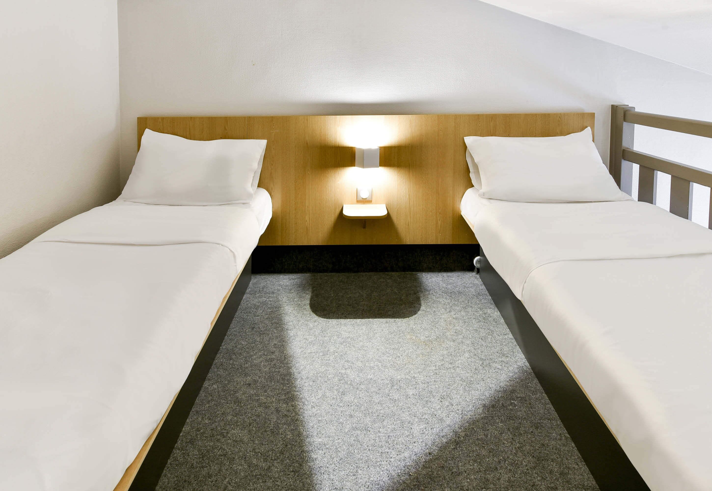 Een tweepersoonskamer met twee bedden, een houten hoofdbord, een nachtlampje en een vloerbedekking.