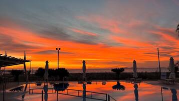 Piscina com vista para o pôr do sol, cadeiras de descanso e céu claro.