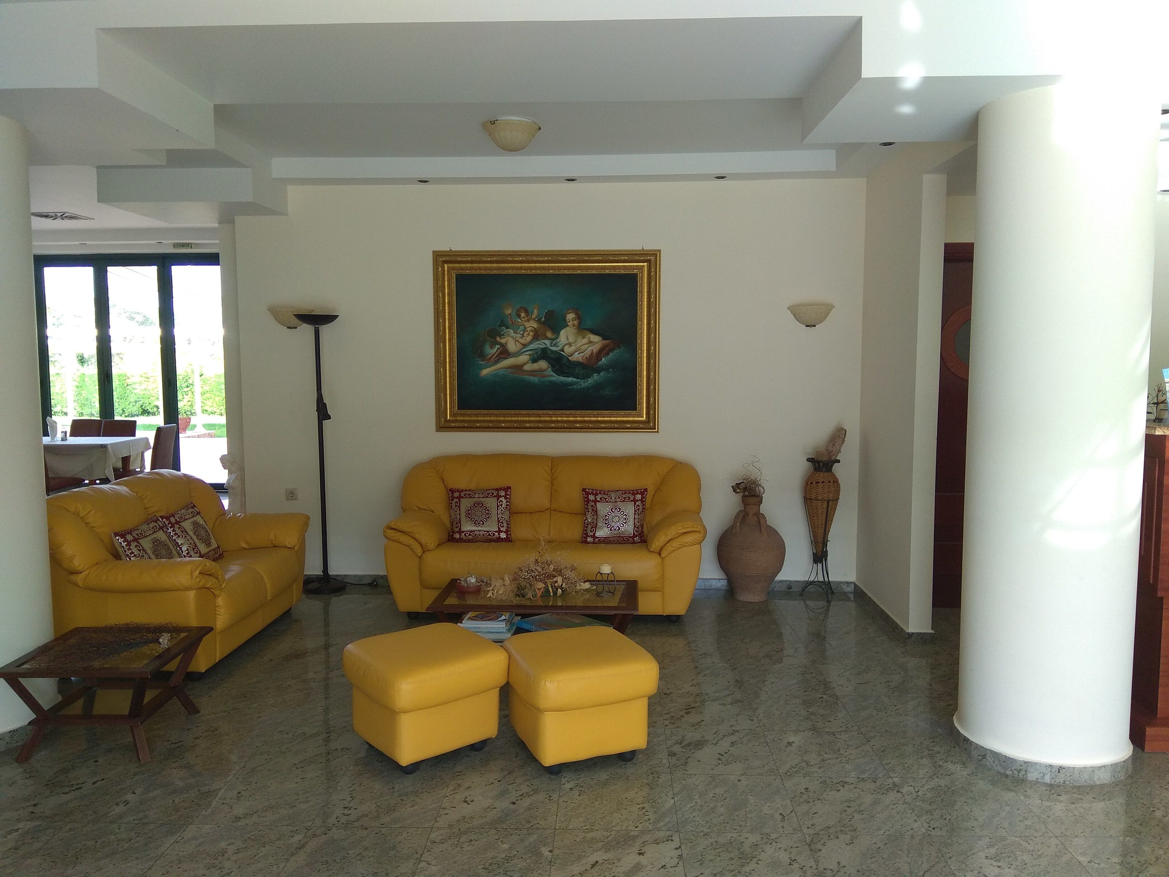 A living room with a yellow sofa, matching ottomans, a coffee table, and a painting on the wall.