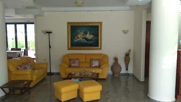 A living room with a yellow sofa, matching ottomans, a coffee table, and a painting on the wall.