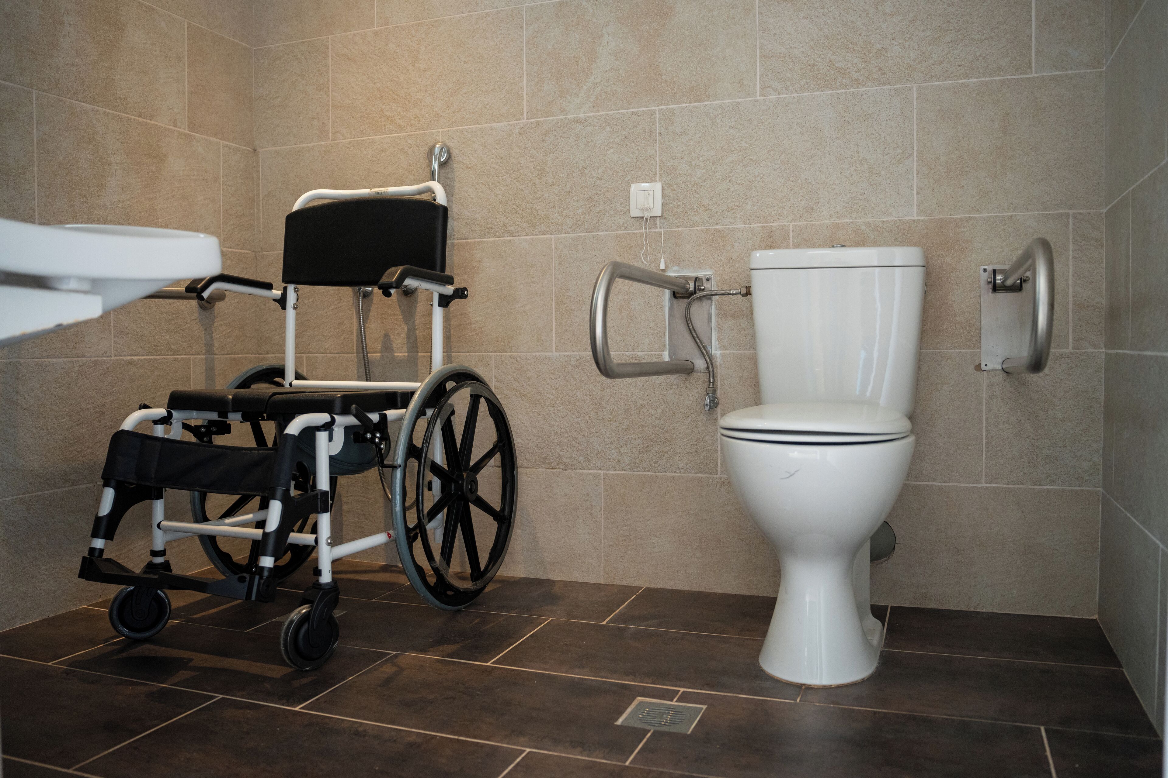 A bathroom with a wheelchair, a toilet, and a shower area.