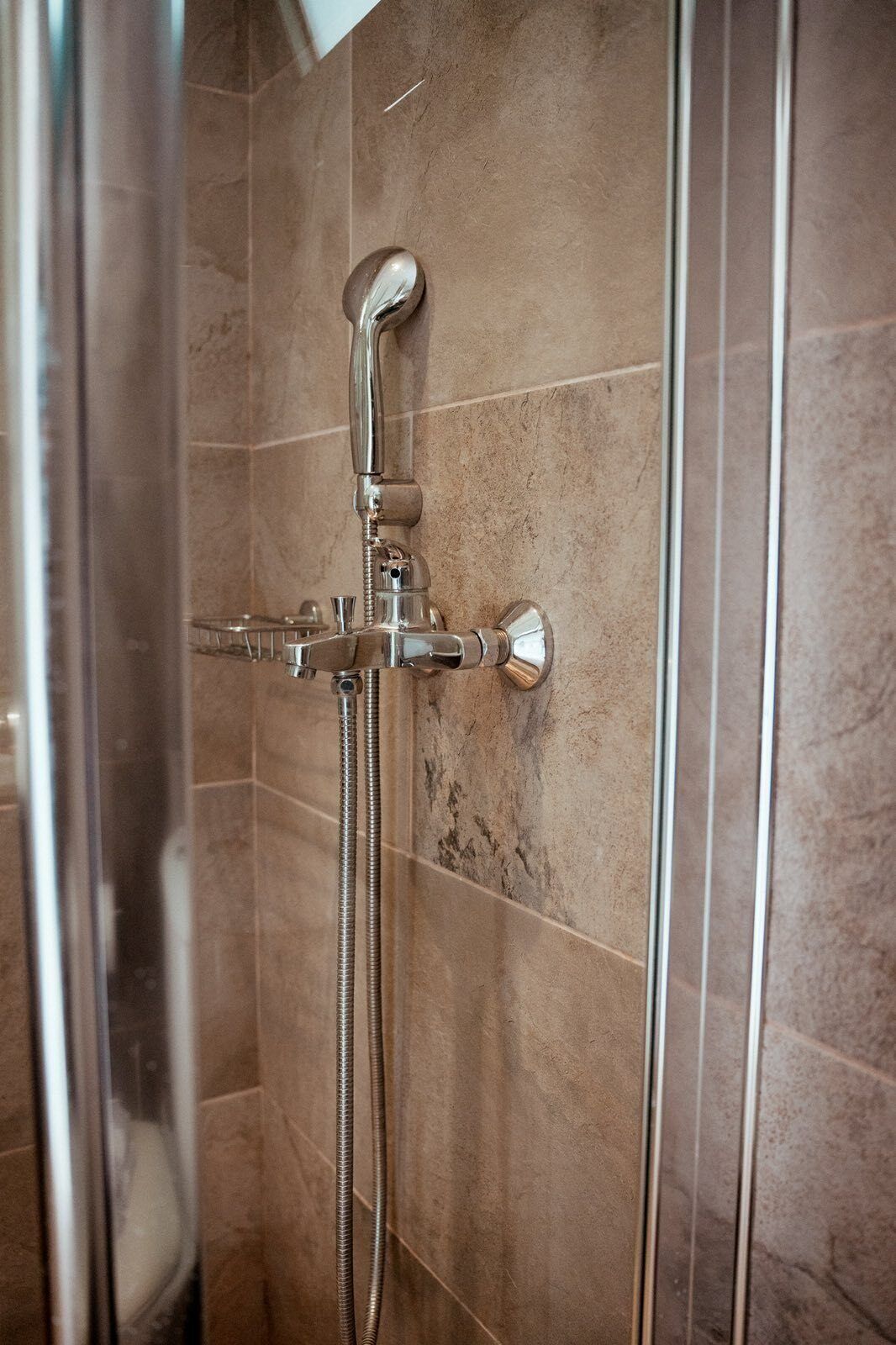 A shower with a handheld showerhead and a fixed showerhead, both mounted on a wall with a tiled surface.