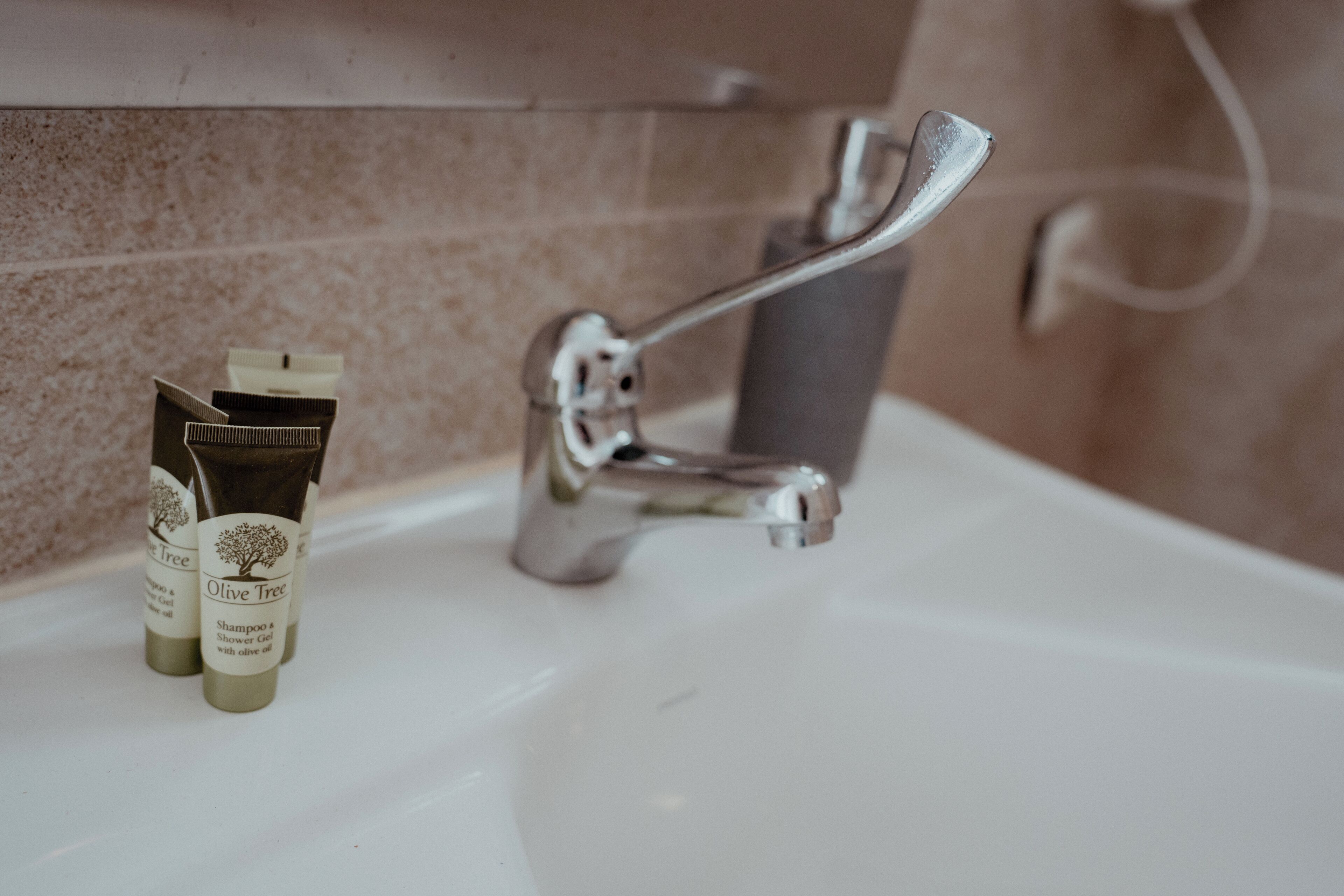 Ein Badezimmerwaschbecken mit chromfarbenem Wasserhahn und zwei Flaschen Shampoo und Duschgel von Olive Tree.