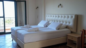 Una cama grande con ropa de cama blanca, una mesita de noche de madera y vistas al exterior a través de una puerta corrediza.