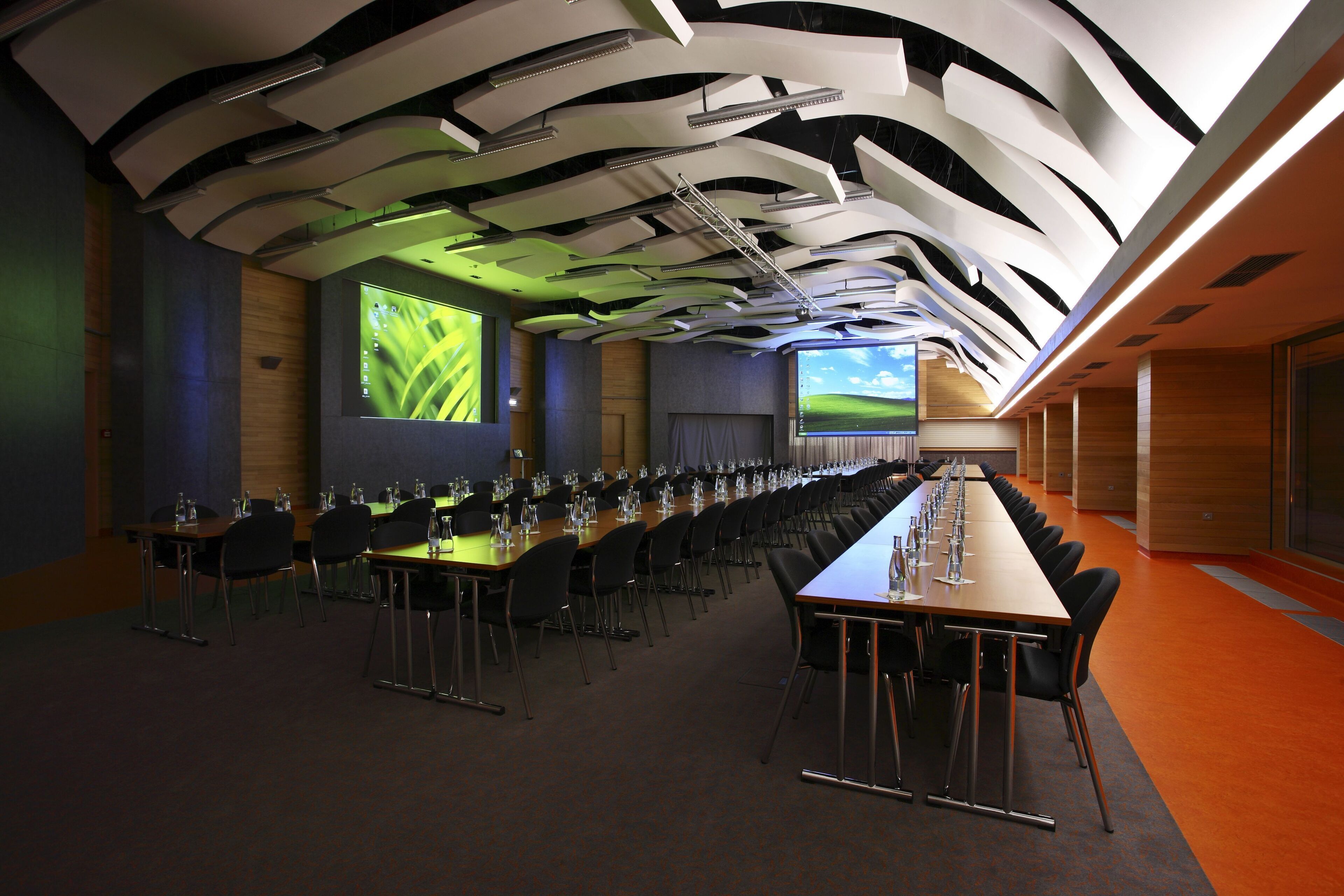 Une salle de conférence équipée d’une longue table, de nombreuses chaises et d’un grand écran diffusant une présentation.