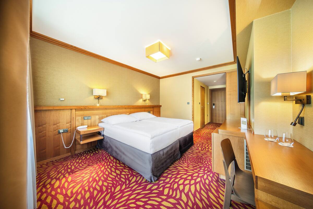 A hotel room with a bed, bedside table, lamp, desk, chair, and a carpeted floor.