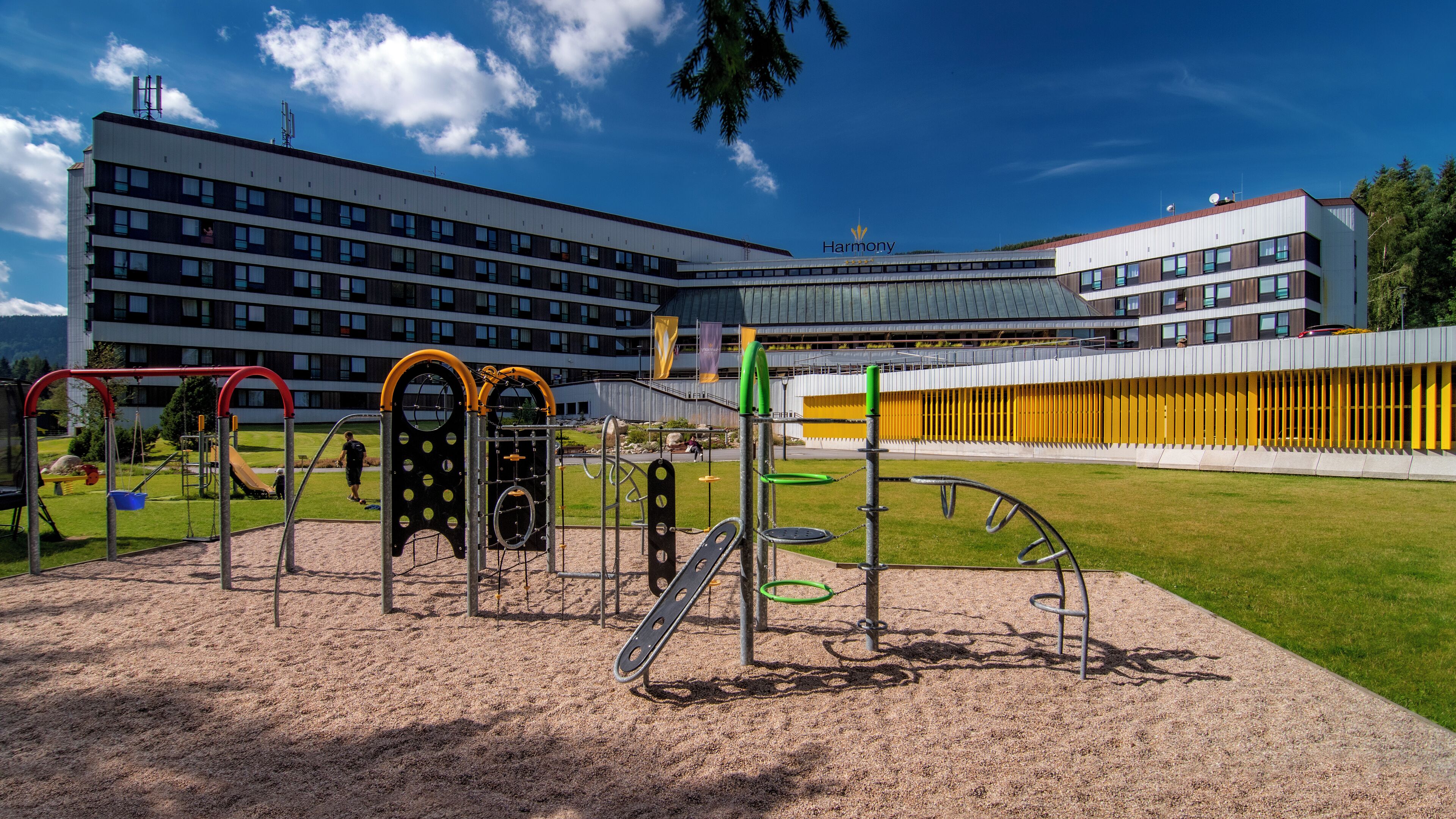 Un parque infantil con diversas estructuras de juego, una zona verde y un edificio con múltiples ventanales al fondo.
