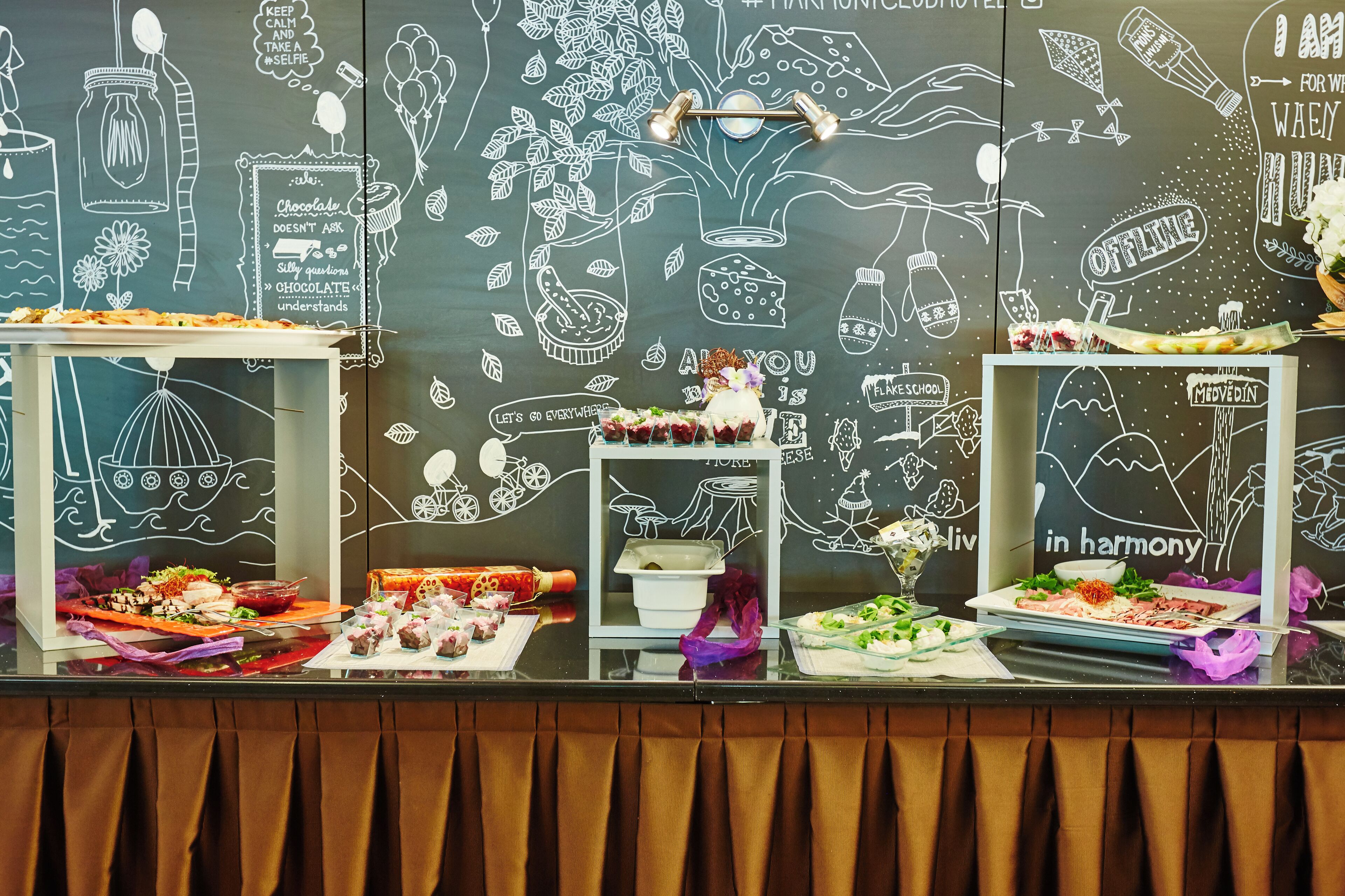 A buffet table with various dishes and a chalkboard wall with food-related drawings and text.