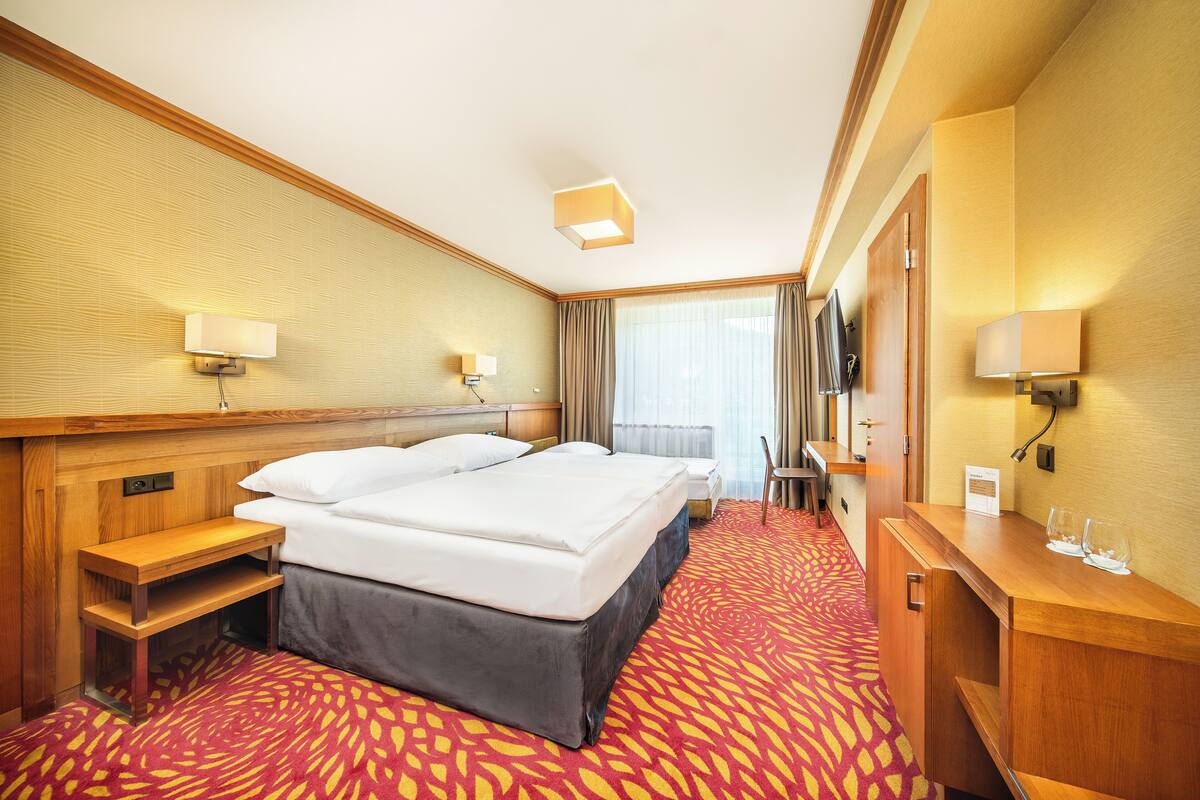 A hotel room with a large bed, bedside tables, a desk, and a mirror.