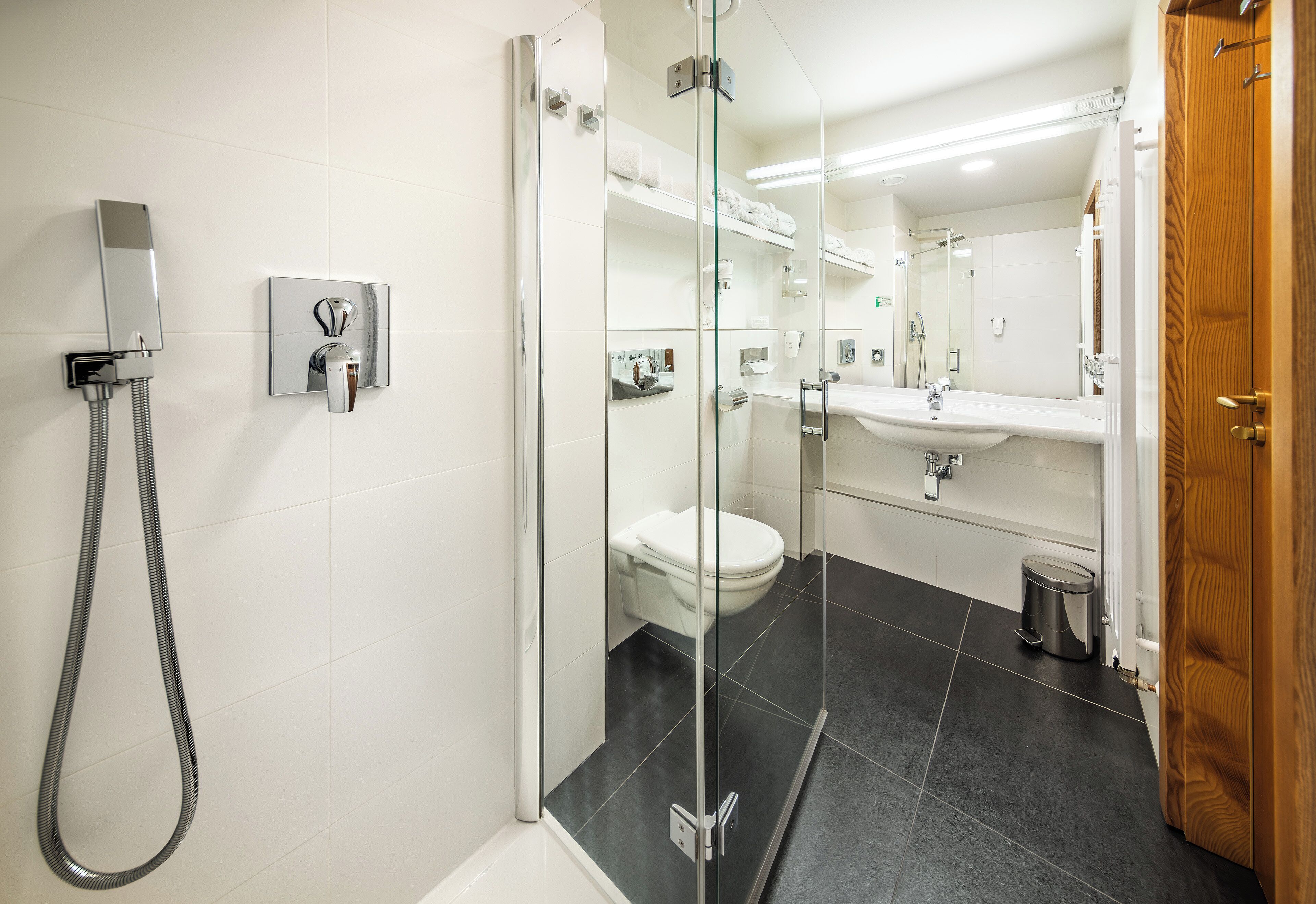 A modern bathroom with a glass-enclosed shower, a white toilet, a sink with a mirror, and a trash bin.
