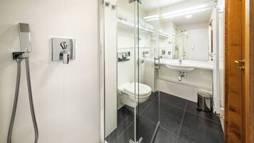 A modern bathroom with a glass-enclosed shower, a white toilet, a sink with a mirror, and a trash bin.