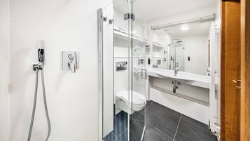 A modern bathroom with a glass-enclosed shower, a white toilet, and a large mirror above the sink.