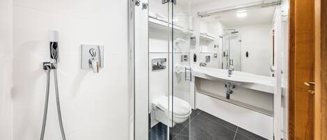 A modern bathroom with a glass-enclosed shower, a white toilet, and a large mirror above the sink.