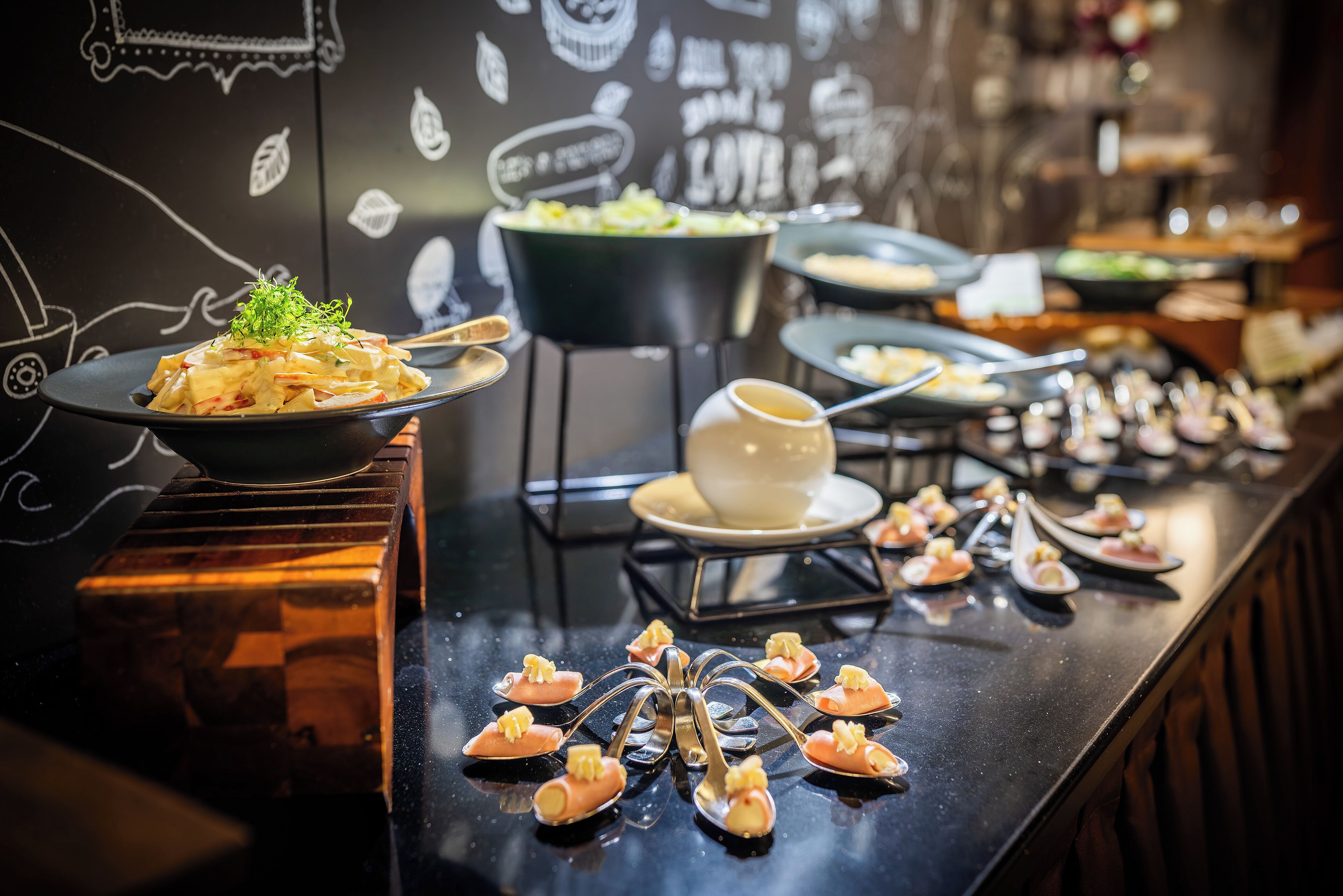 A buffet with various dishes and a decorative wall with white drawings.