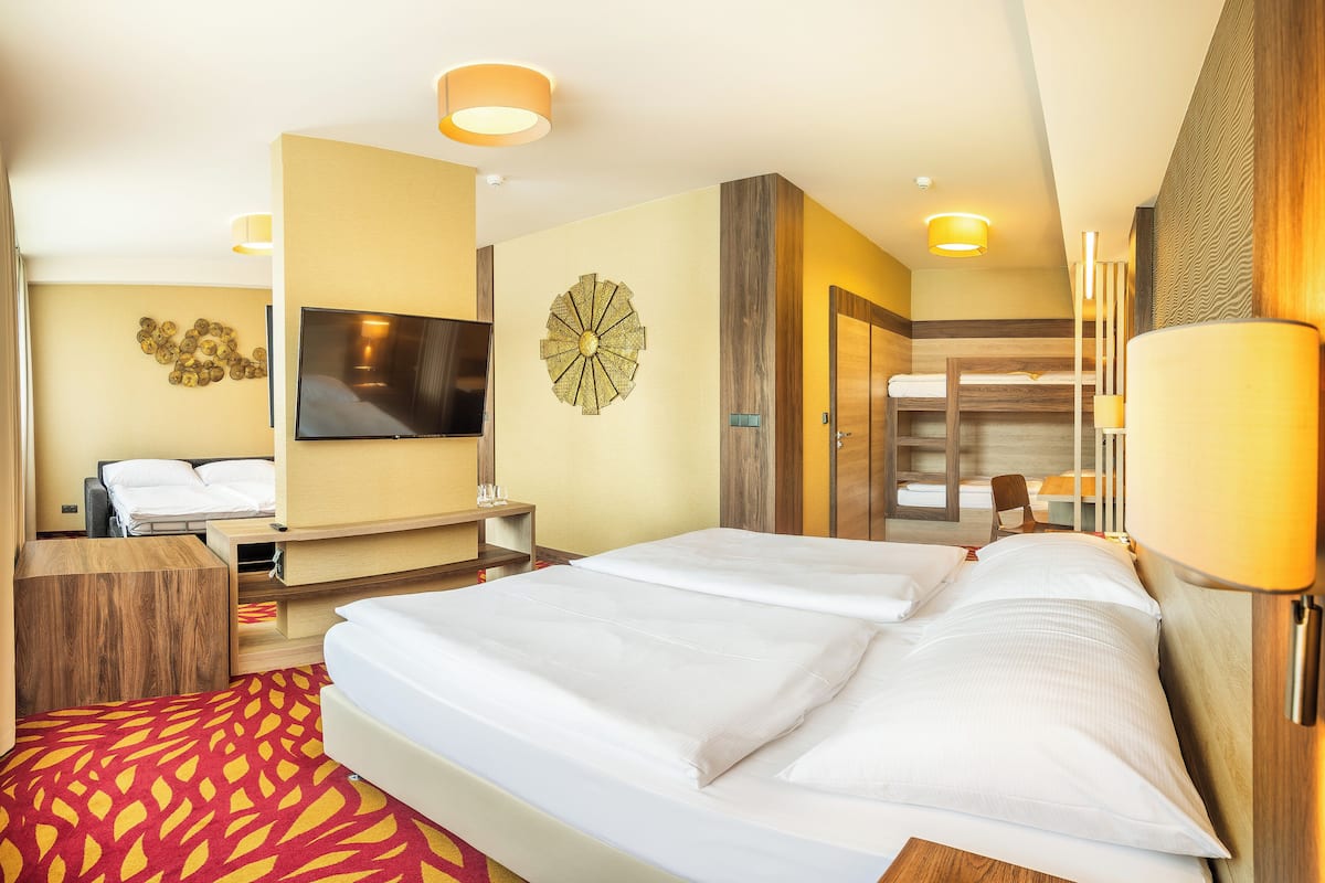 A hotel room with a large bed, a TV, a wall-mounted decorative piece, and a wooden wardrobe.