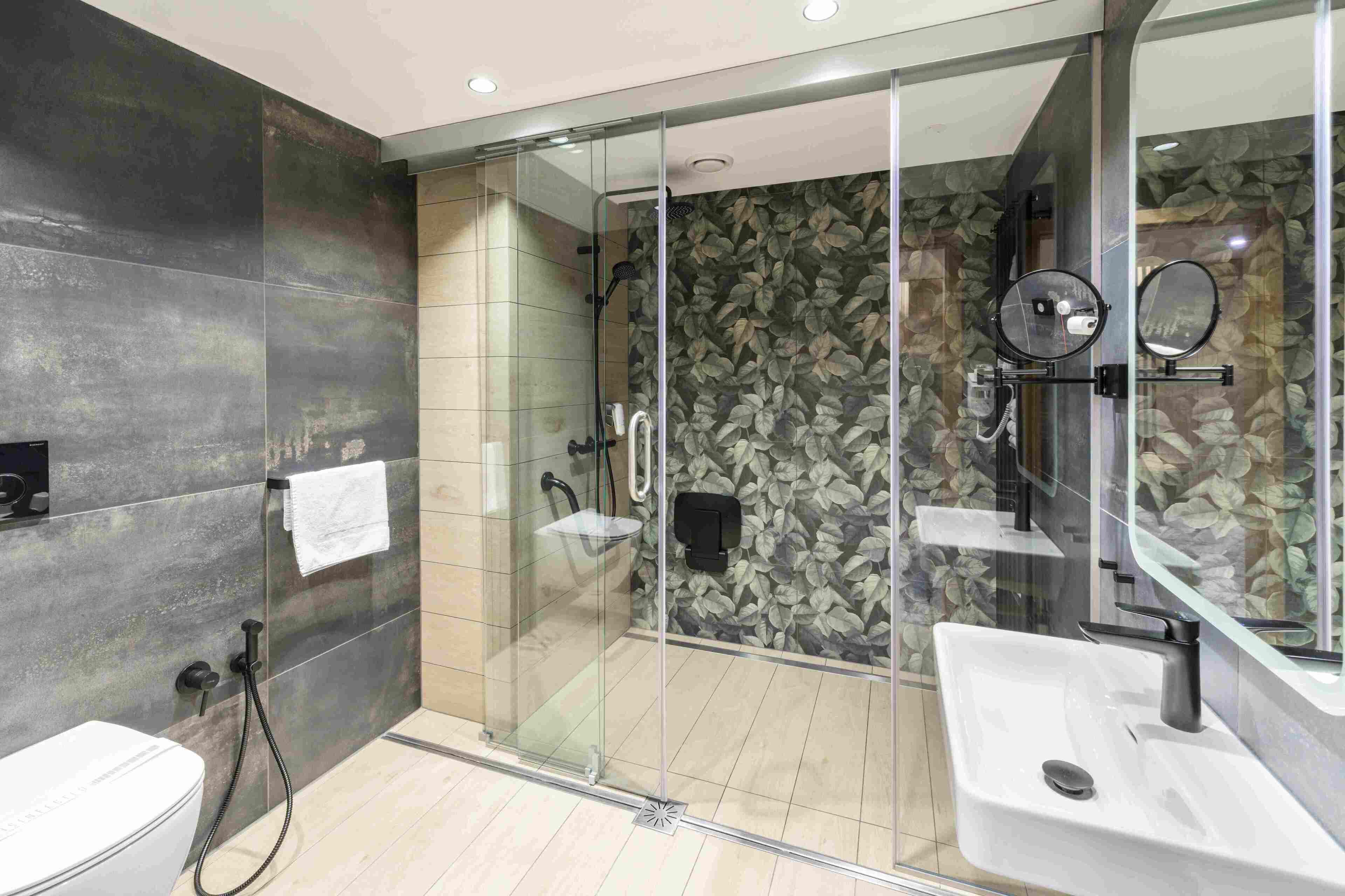 Un baño moderno con ducha envuelta en vidrio, un lavamanos blanco y un espejo grande.