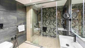 Un baño moderno con ducha envuelta en vidrio, un lavamanos blanco y un espejo grande.
