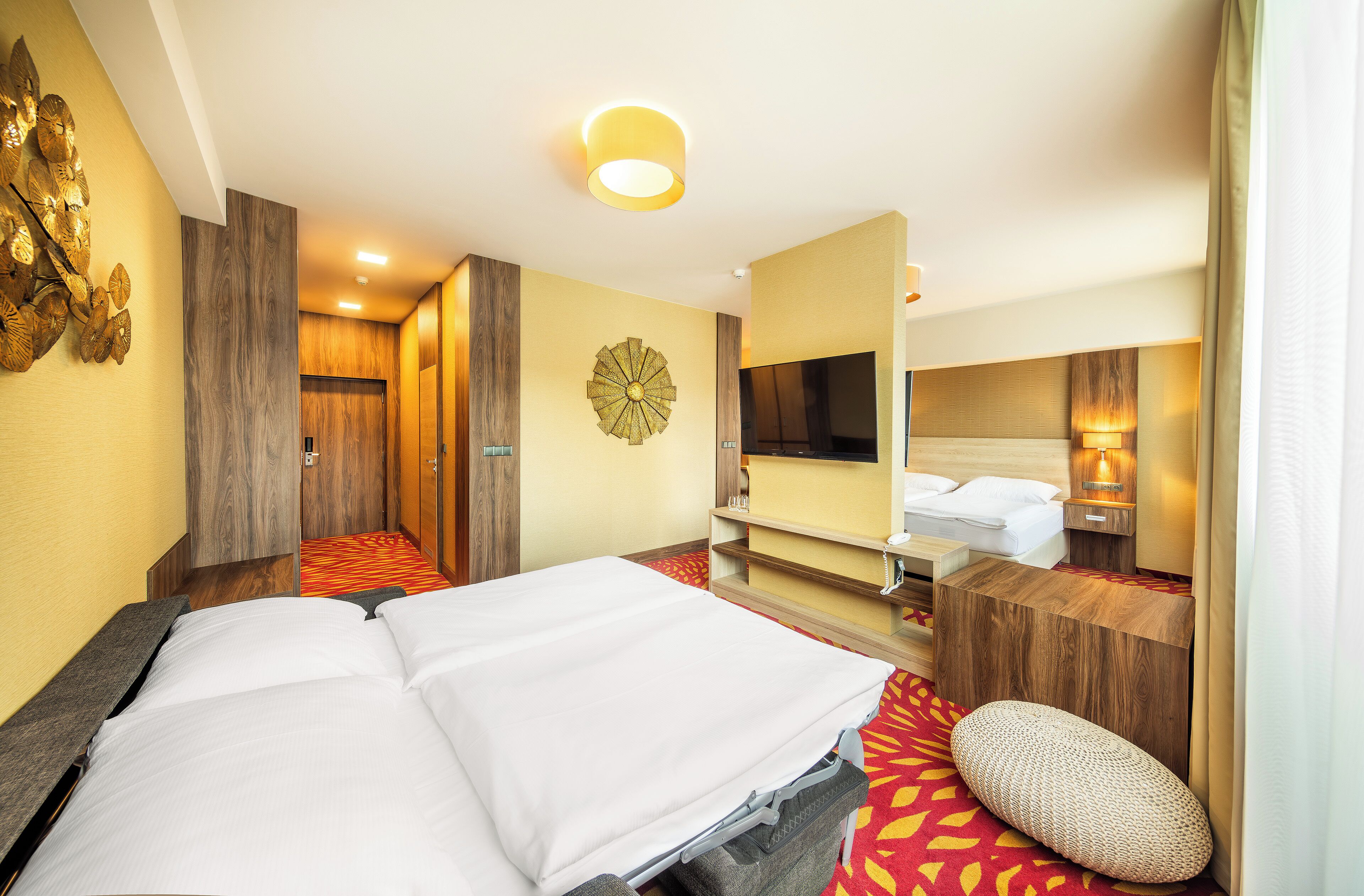Een hotelkamer met een bed, een nachtkastje van hout, een spiegel, een wandklok en een televisietoestel.