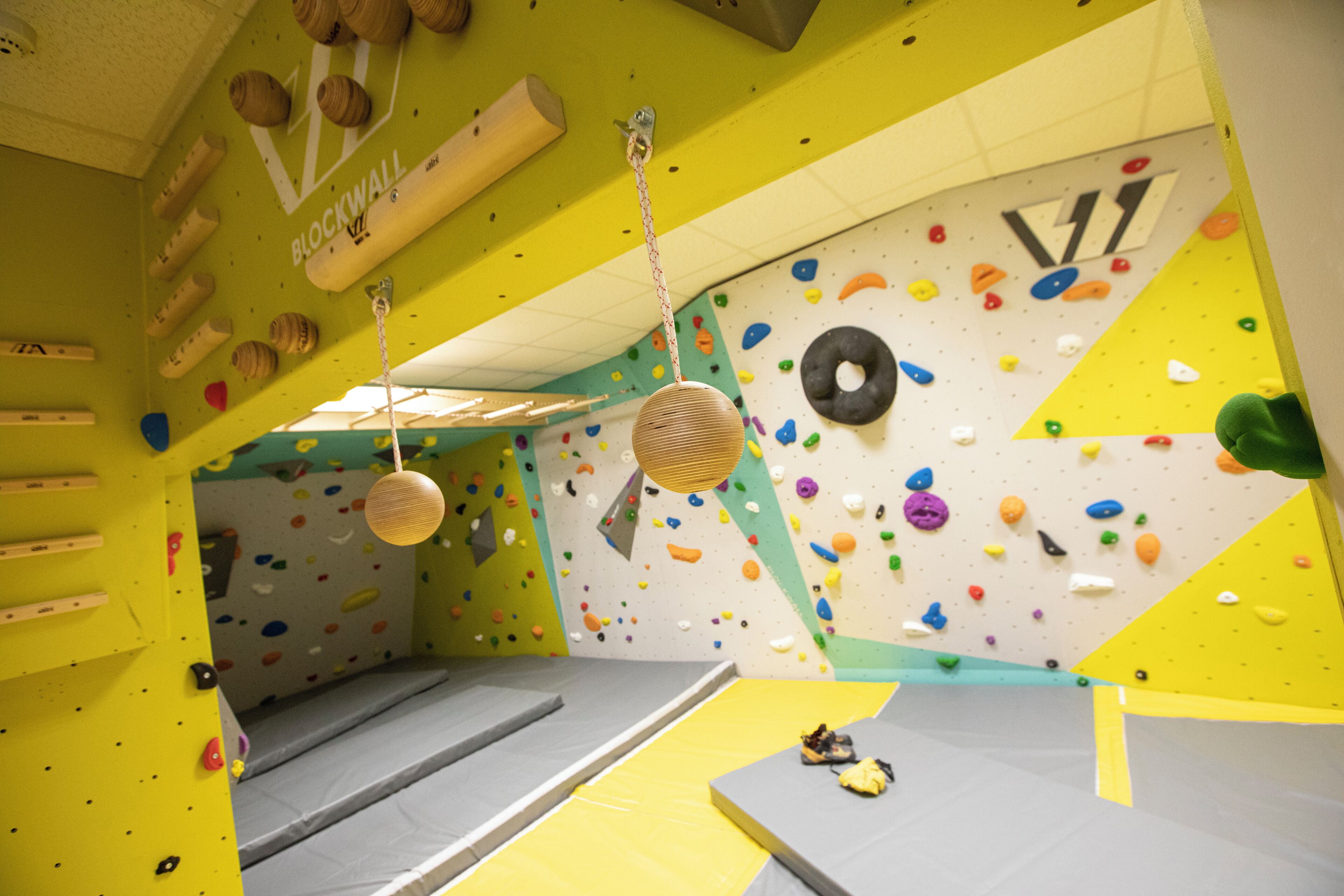 Un gimnasio de escalada en interiores con suelos acolchados, paredes de escalada de colores y diversos puntos de agarre.