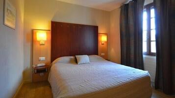 Una habitación de hotel con una cama grande, dos lámparas de noche, una mesita de noche y una ventana con cortinas.