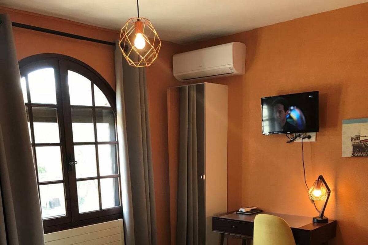 A hotel room with a bed, a desk, a chair, a television, and an air conditioning unit.