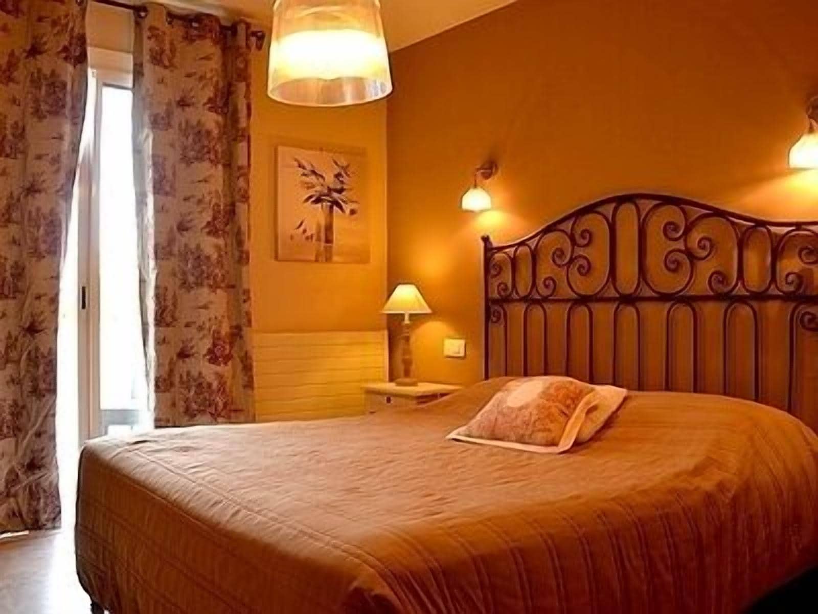 A bedroom with a large bed, a nightstand, a lamp, and a wall-mounted light fixture.