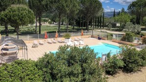Un espace piscine doté de chaises longues et de parasols, entouré d’arbres et d’un jardin clos.