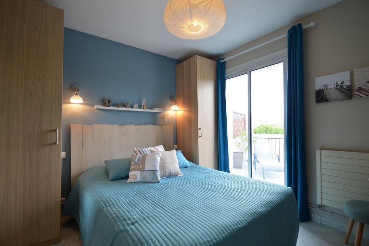 A bedroom with a bed, a wardrobe, a shelf with toiletries, and a view of the outdoors.