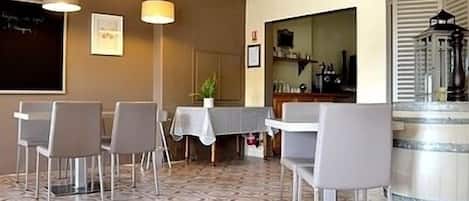 A dining area with a patterned floor, a table with chairs, pendant lights, and a clock on the wall.