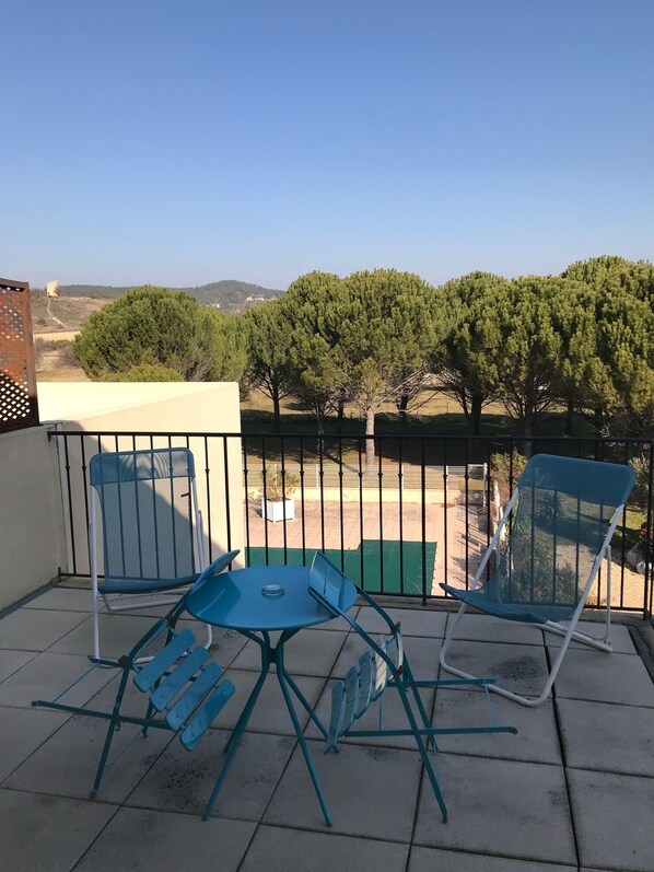 Un balcón con una mesa y dos sillas, con vistas a un paisaje de árboles y colinas.