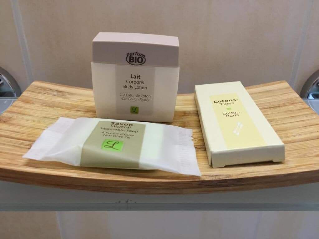 Una bandeja de madera con tres productos para el cuidado de la piel: una loción corporal, una pastilla de jabón y una caja de bastoncillos de algodón.