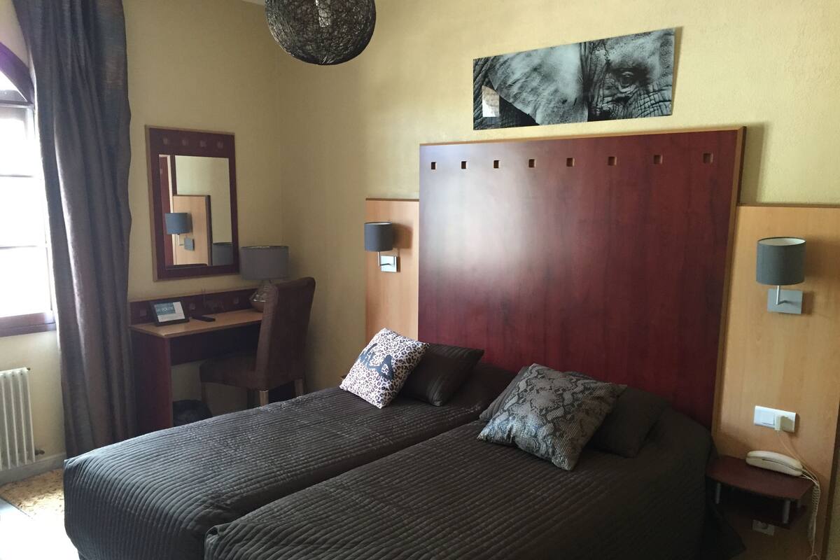 A hotel room with a double bed, a desk with a chair, a mirror, and a telephone.