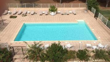 A rectangular swimming pool with lounge chairs and a small garden area.