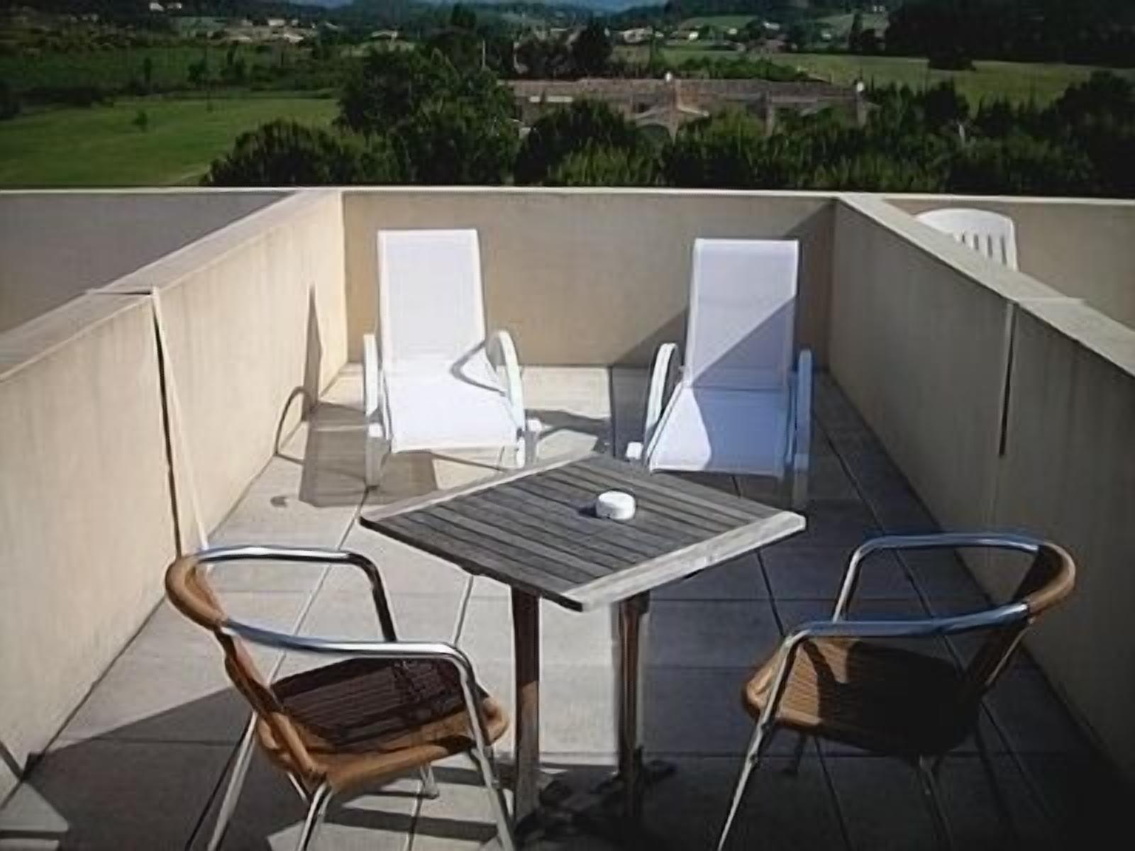 Un balcone con un tavolo e due sedie, vista su un paesaggio verde.