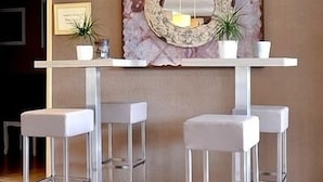 Un espace bar moderne avec deux tabourets de bar blancs, un miroir décoratif et deux plantes en pot.
