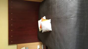 Una habitación de hotel con una cama grande, un cabecero de madera, una mesita de noche con lámpara y un teléfono instalado en la pared.