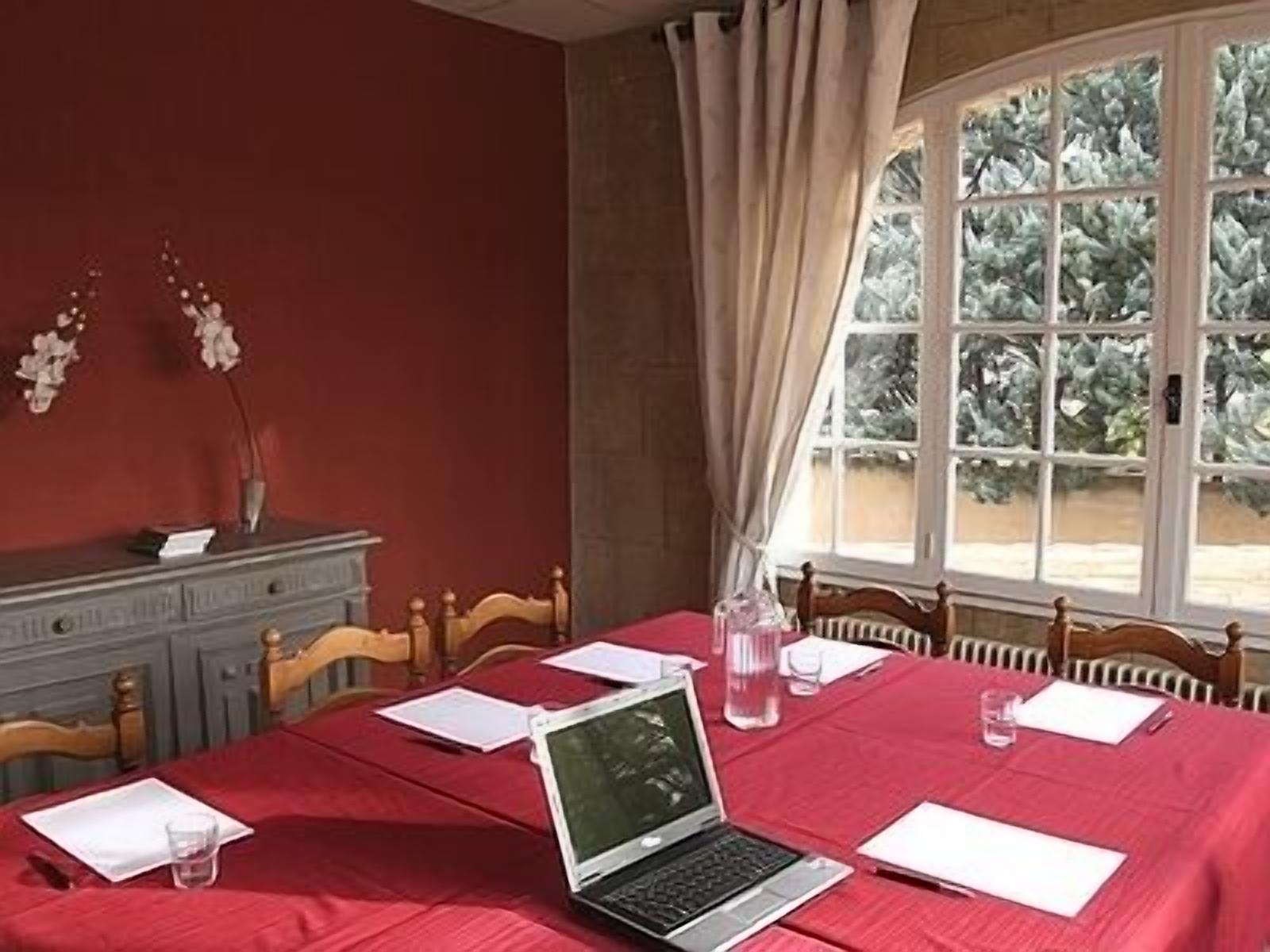 A dining area with a red tablecloth, a laptop, papers, and a vase with flowers.
