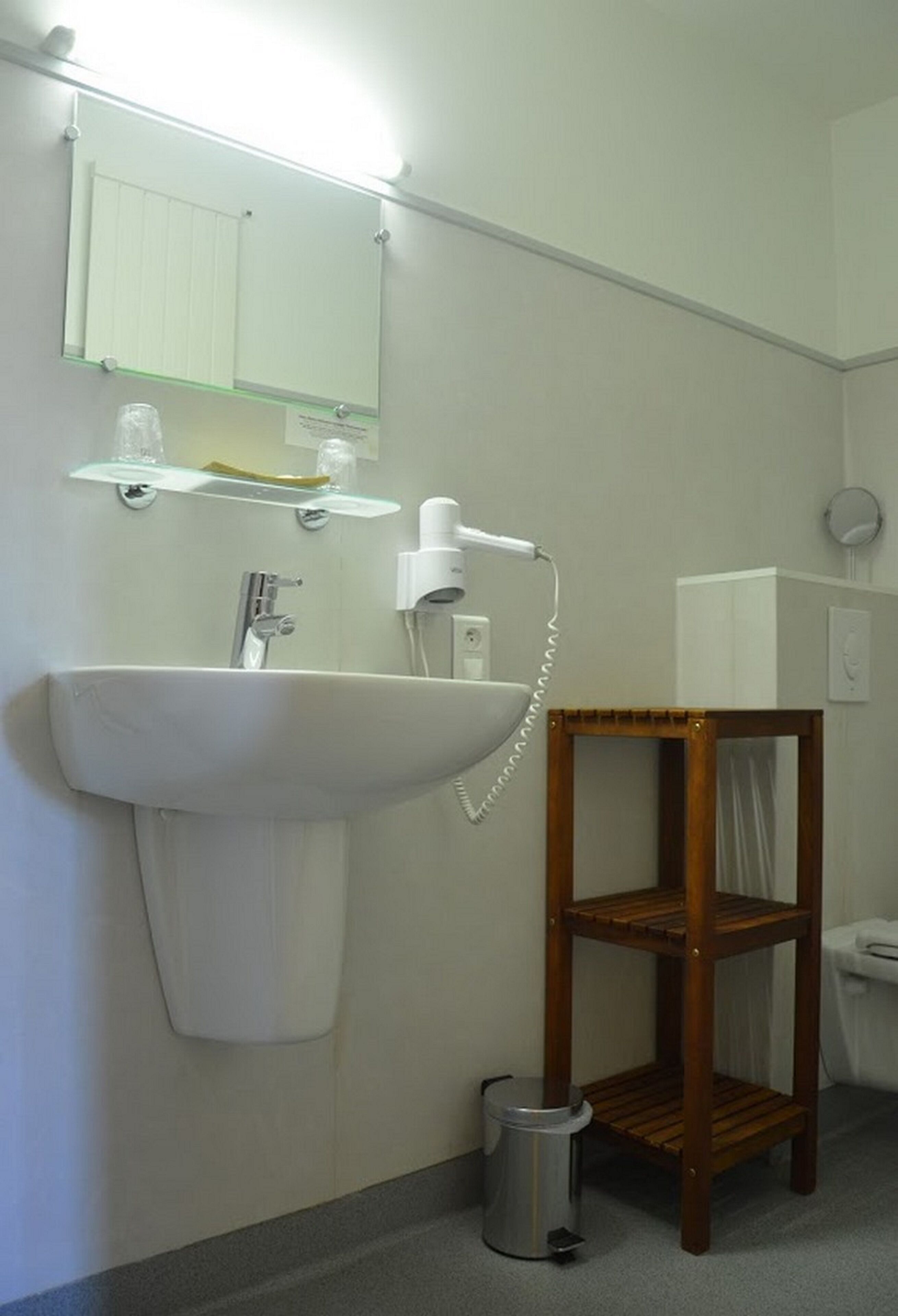 A bathroom with a sink, mirror, and a wooden shelf.