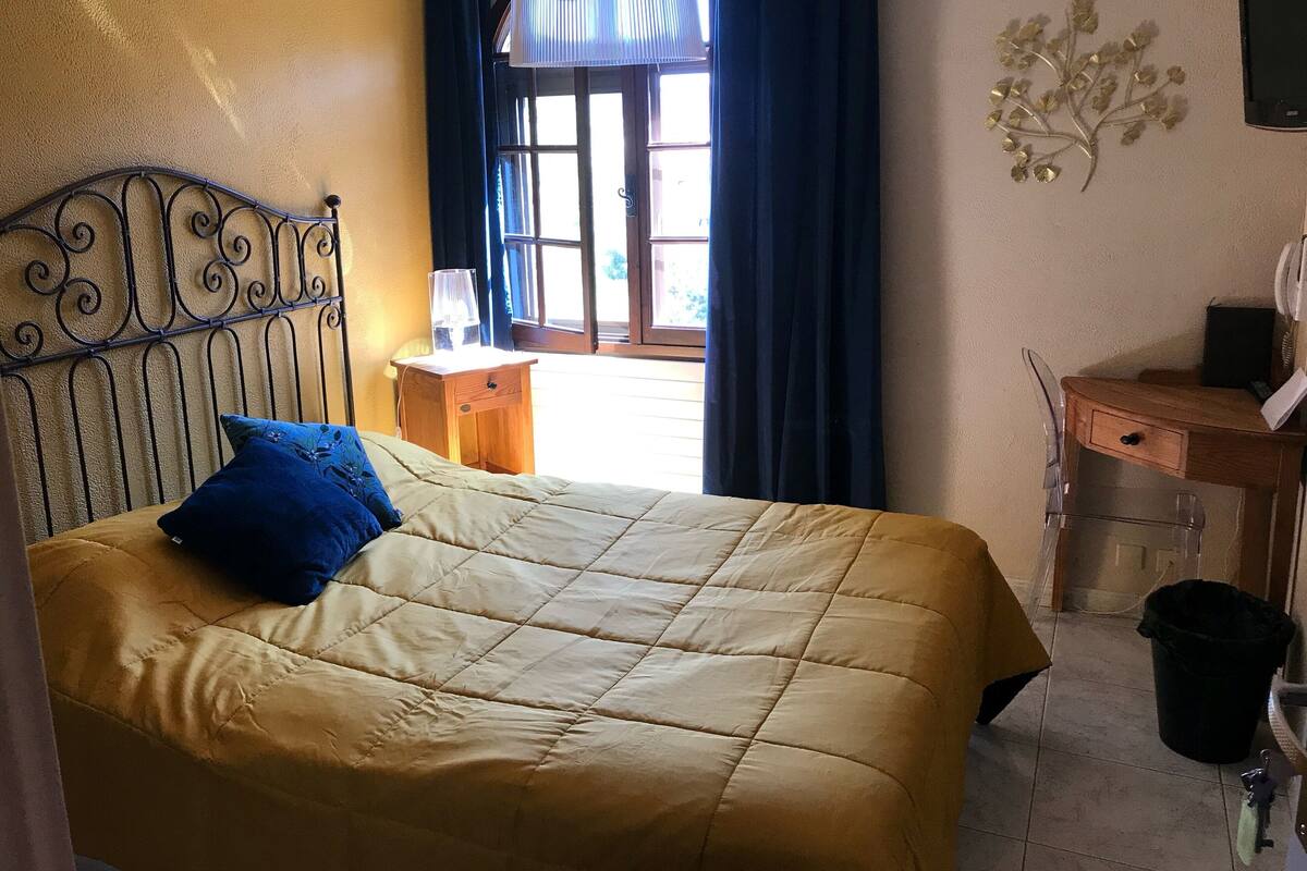A bed with a yellow quilt, a blue pillow, and a wooden nightstand with a lamp.