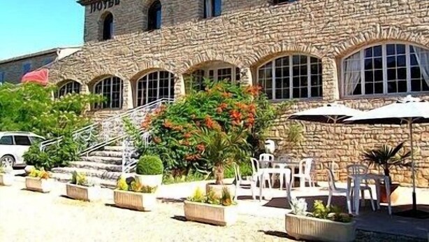 Un bâtiment en pierre doté de fenêtres en arc de cercle et d’une enseigne indiquant « HÔTEL-RESTAURANT ».