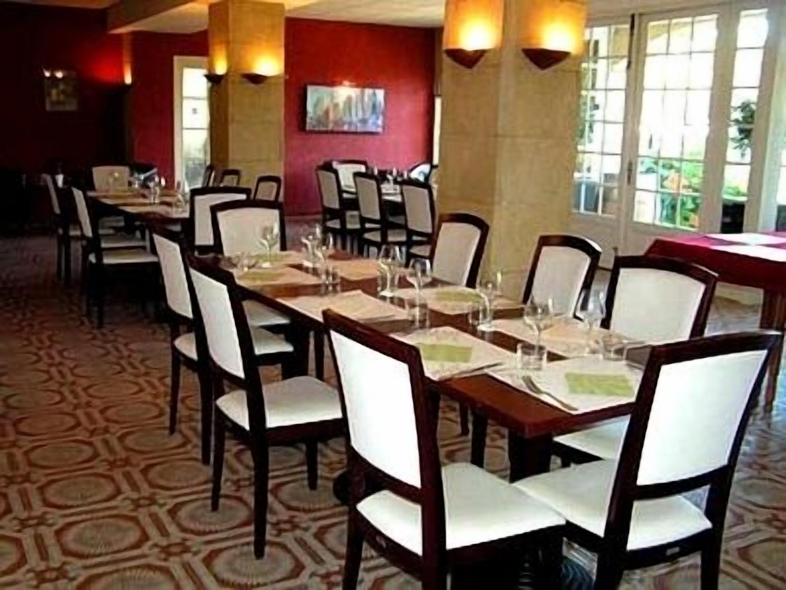 Un comedor con mesas largas dispuestas para varios comensales, sillas y una alfombra estampada.