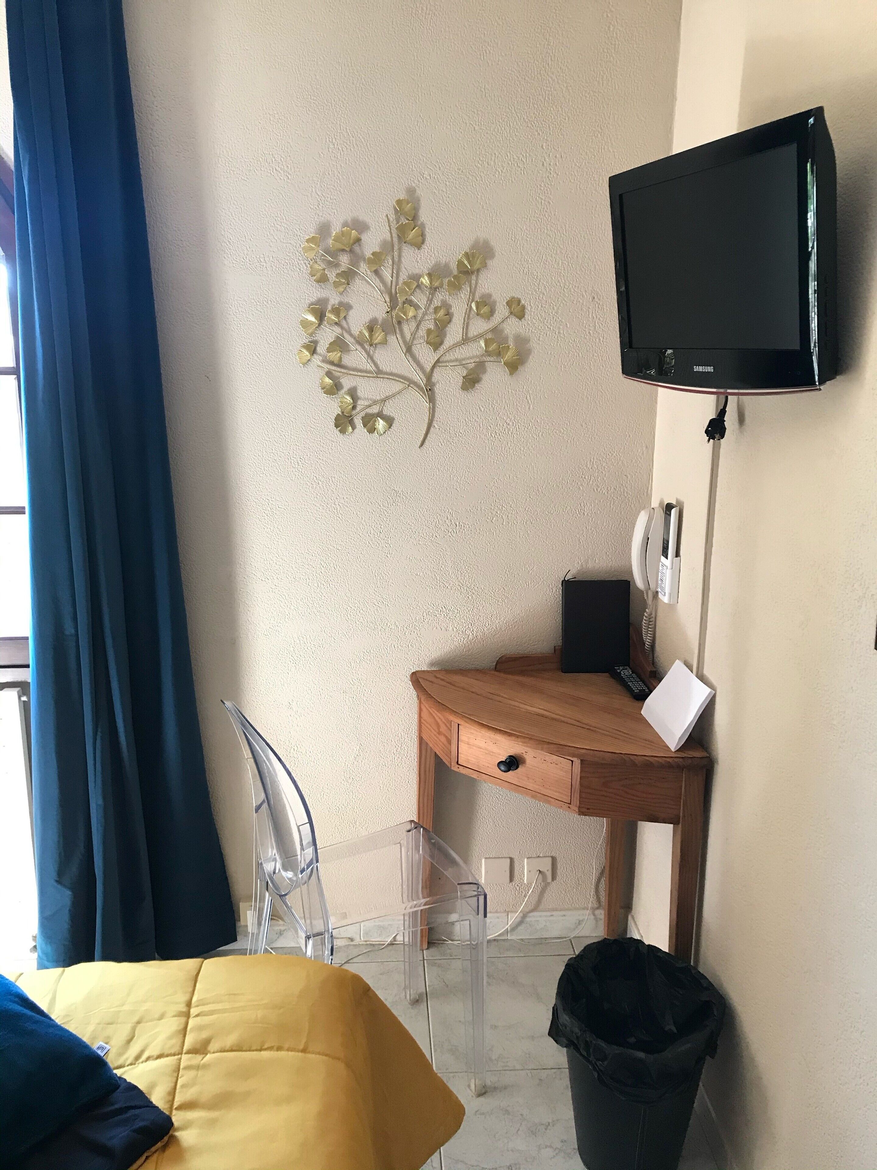 Habitación de hotel con cama, escritorio con silla, televisor y teléfono instalado en la pared.