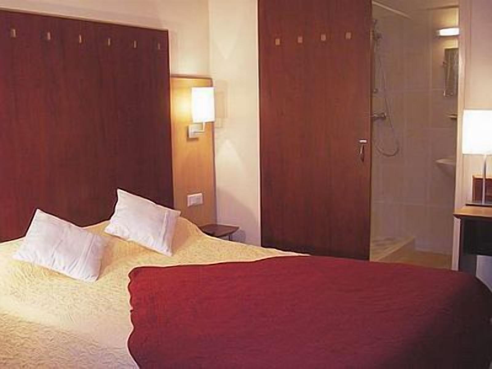 A hotel room with a bed, a nightstand, a lamp, and a shower area.