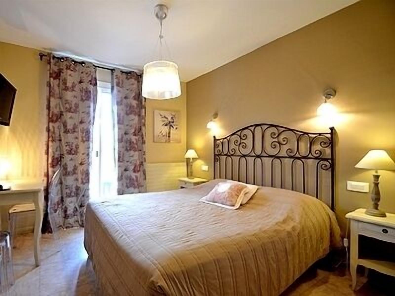 Una camera da letto con un letto, due comodini con lampade, una sedia, una finestra con tende e un'opera d'arte appesa al muro.
