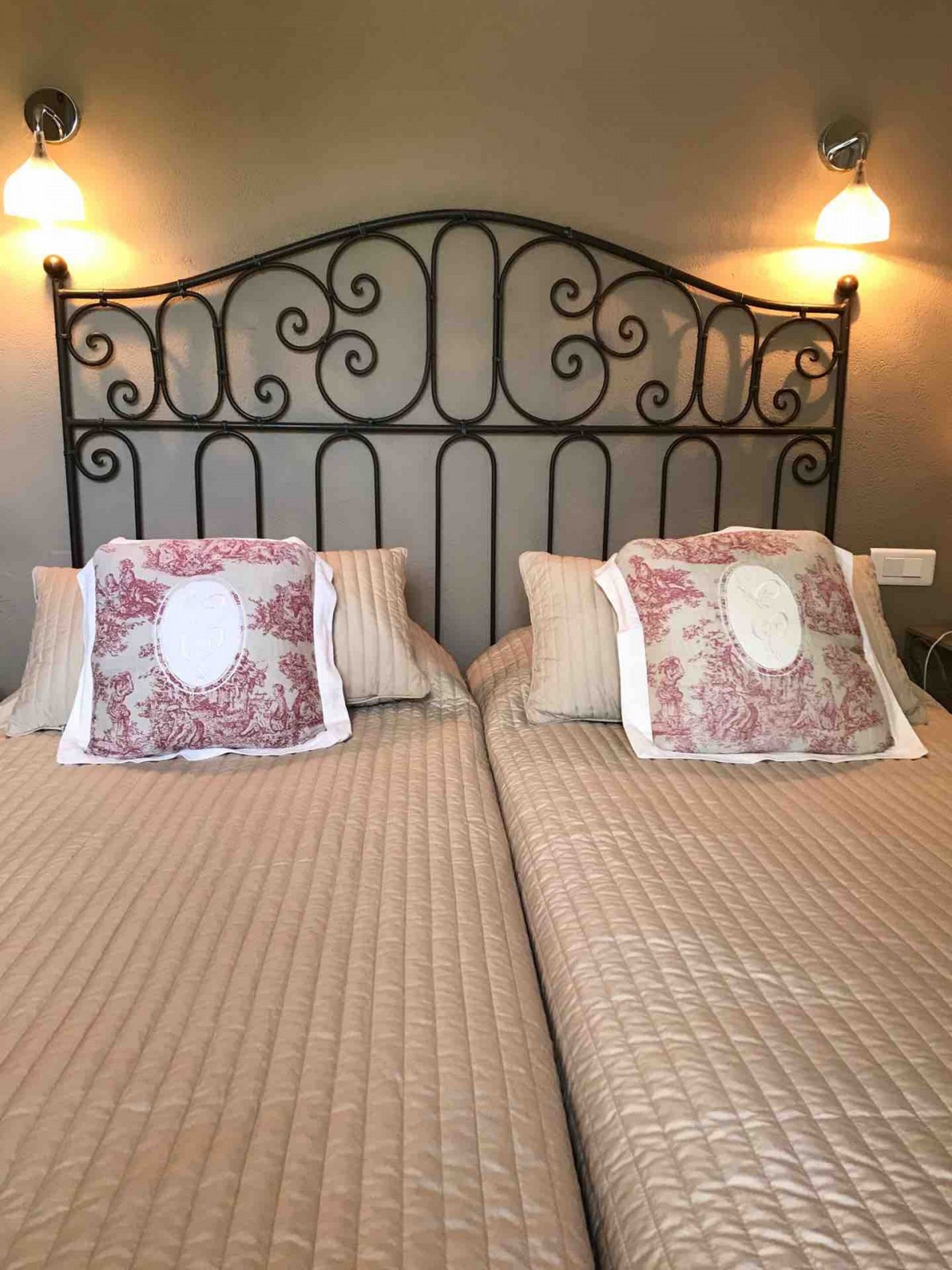 Dos camas con cabeceras a juego y almohadones decorativos, una lámpara de pared y un enchufe.