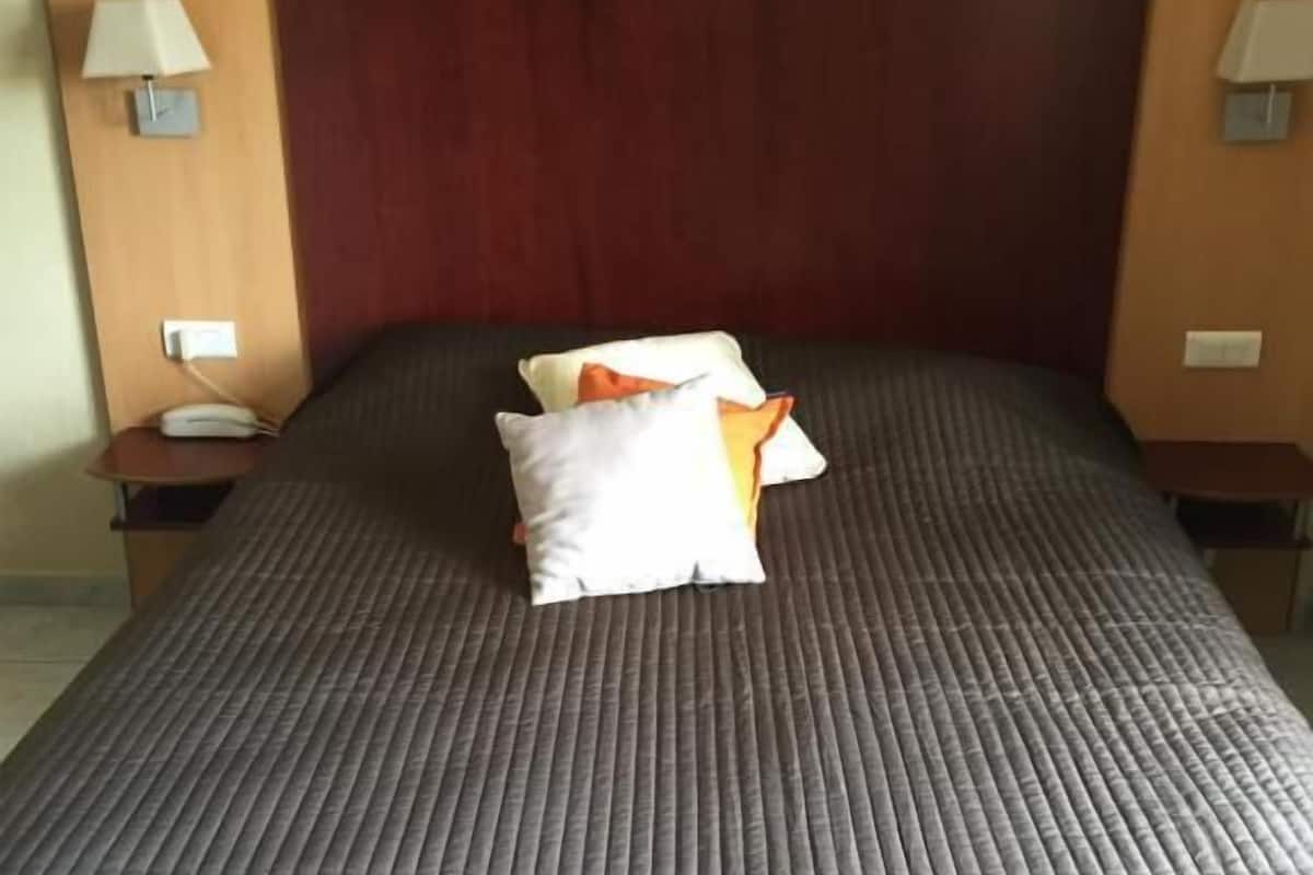 A hotel room with a large bed, a wooden headboard, and two bedside tables with lamps.