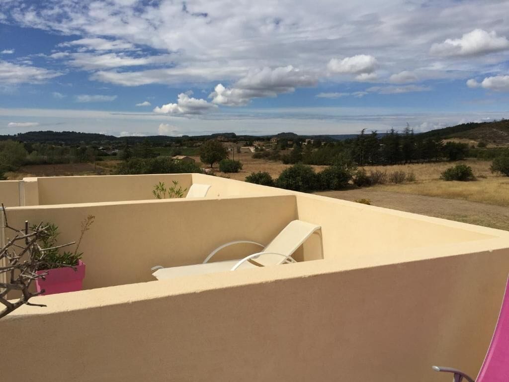 Una terraza en la azotea con un muro color beige, una jardinera rosa con un pequeño árbol y una silla blanca.