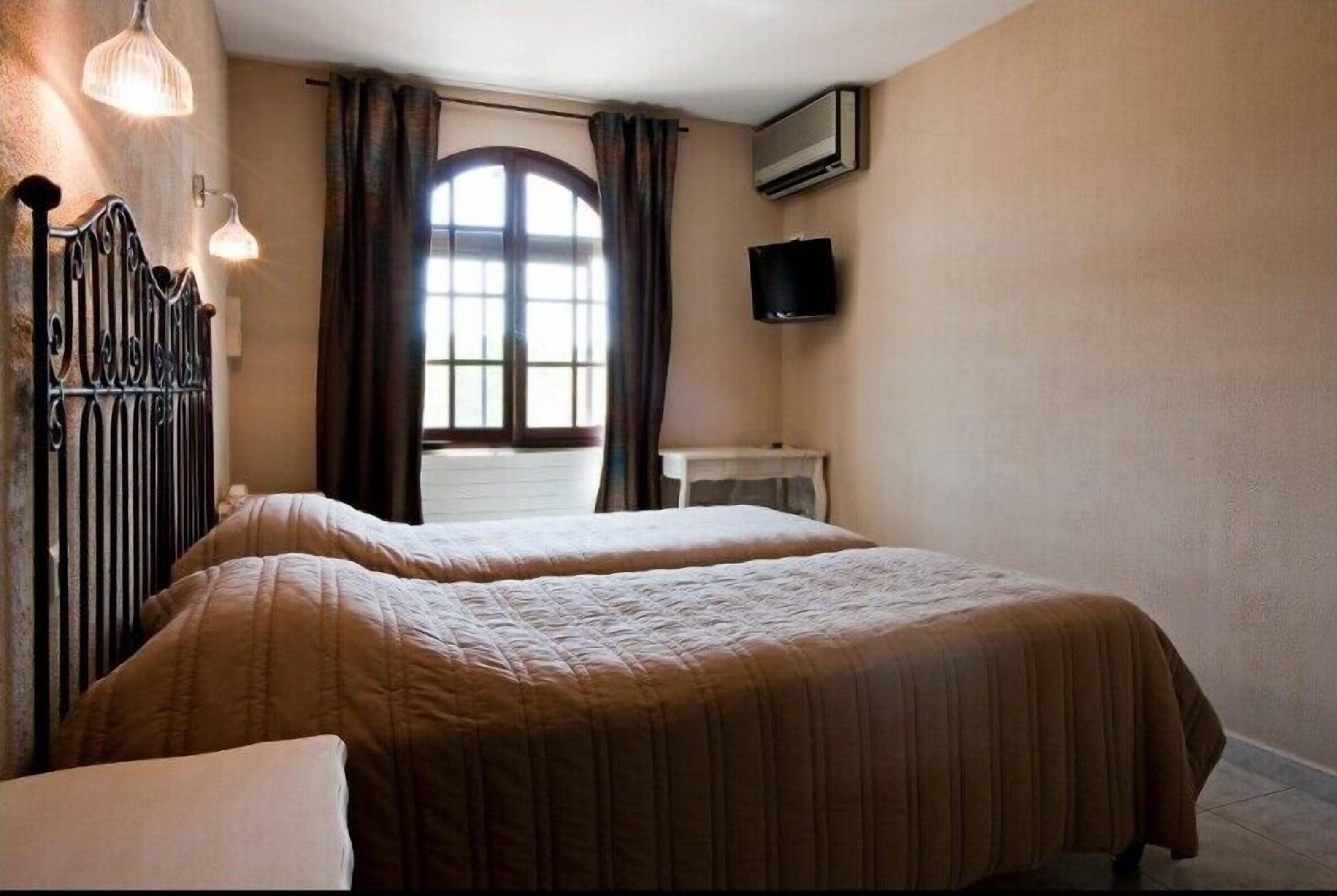 A bedroom with two beds, a window with curtains, a flat-screen TV, and an air conditioning unit.