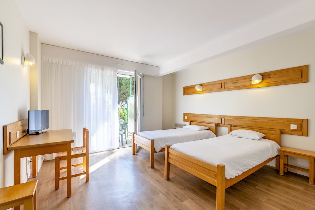 Una habitación con dos camas de madera, un escritorio y una televisión.